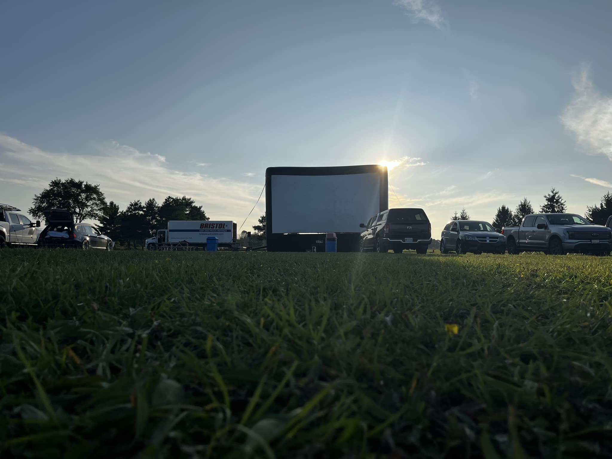an inflatable movie screen in a grassy field with a sunset.