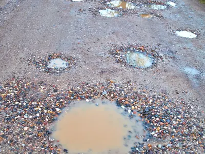 a gravel road with puddles and potholes