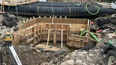 Construction site for a bridge project showing completed excavation and wooden formwork with steel rebar in place for the foundation.