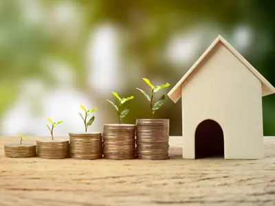 stacks of coins with plants and a wooden house