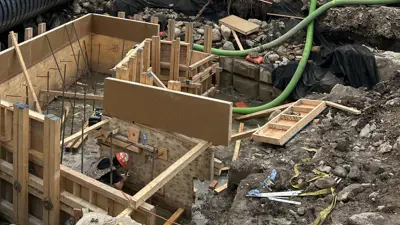 Construction site for a bridge project showing completed excavation and wooden formwork with steel rebar in place for the foundation.